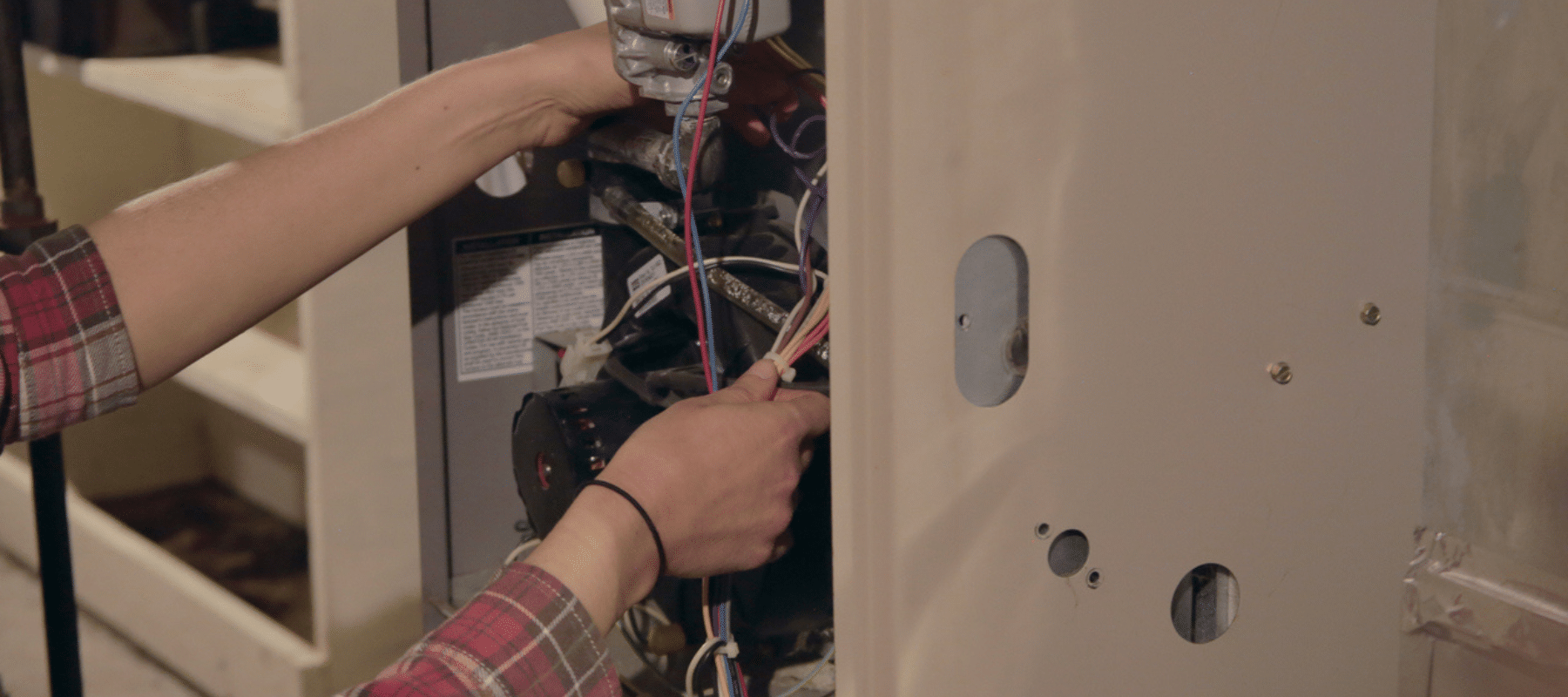 Technician inspecting and adjusting wires inside a home heating system for maintenance